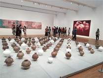 相片：126件白色和褐土色的陶瓶展品在地上分行排列。