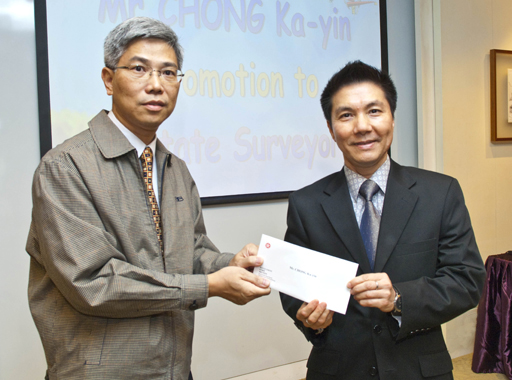 相片：晉升為產業測量師的莊家然(左)獲副署長(屋邨管理)李國榮頒授升職賀函。	