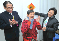 相片∶房委会主席郑汝桦(右)探访元州邨长者住户，为她贴上自己所写的挥春。左为安老事务委员会主席梁智鸿医生。